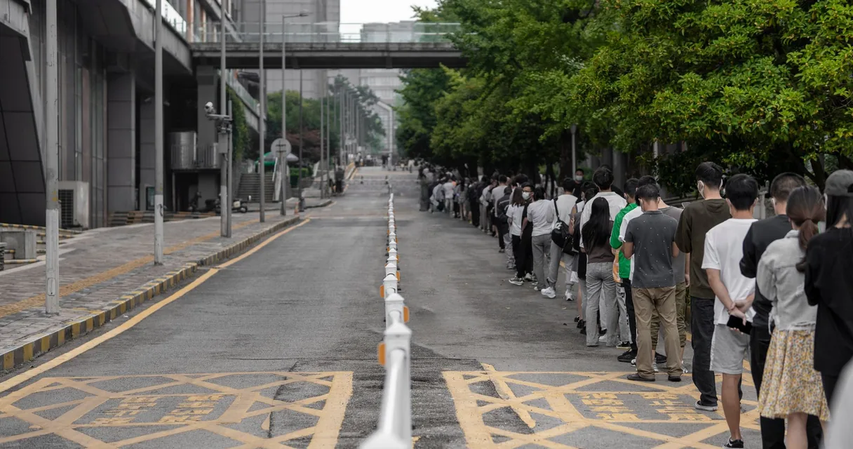 Fila longa de pessoas em uma calçada à espera de atendimento em um prédio público